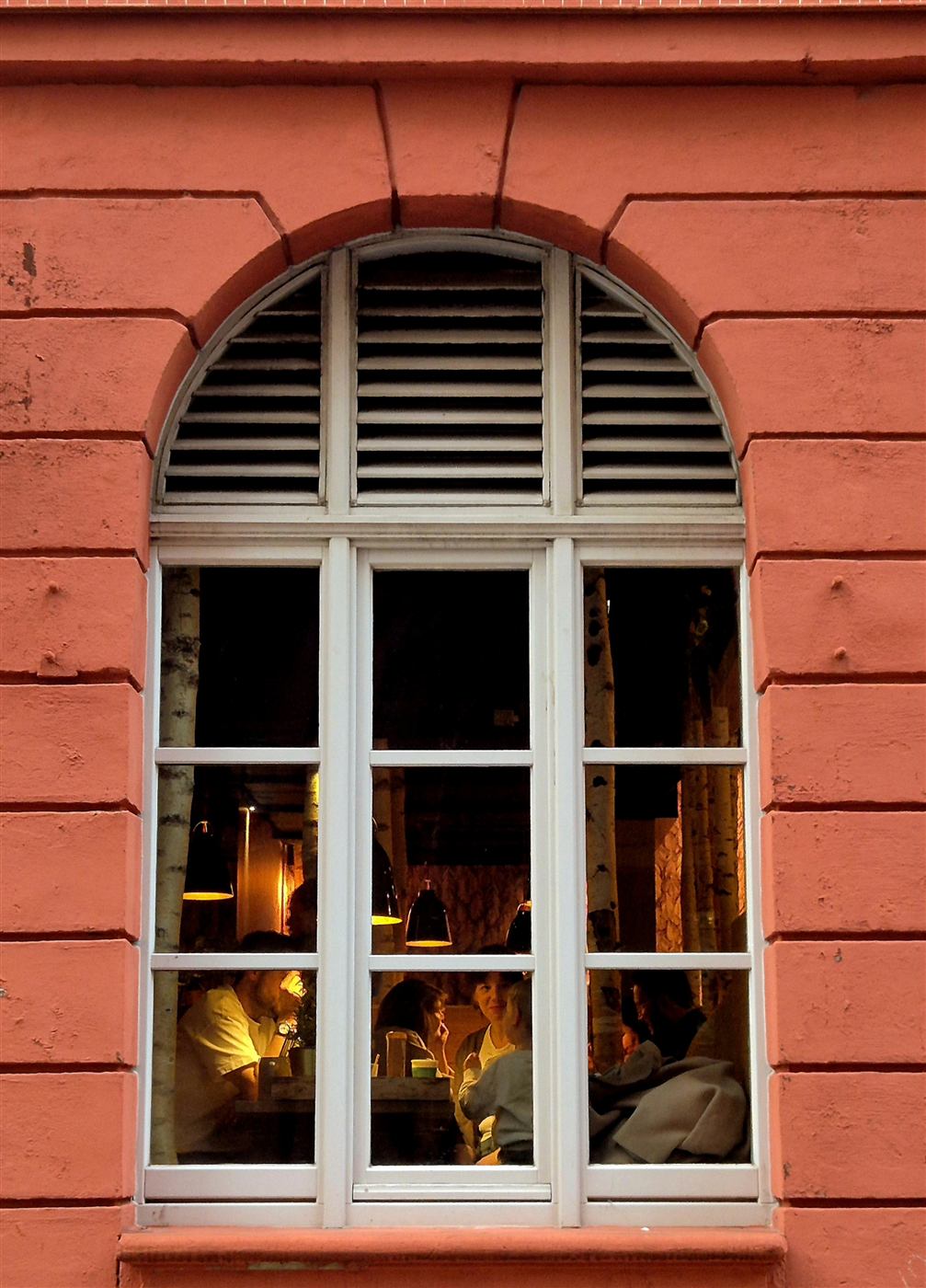 An arched window in a red facade, lit from inside