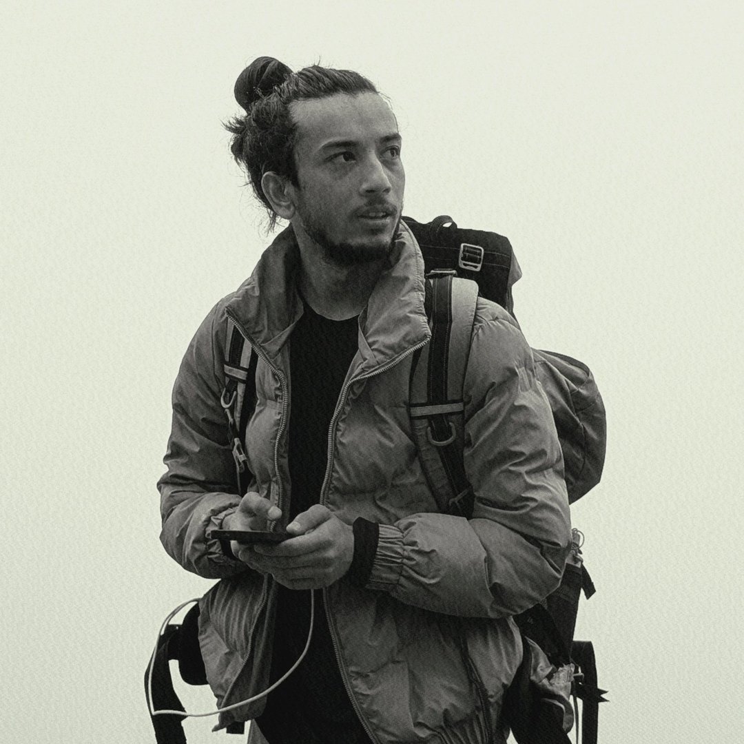 Black-and-white portrait of Suman Pathak in a puffer jacket with a backpack, outdoors in fog